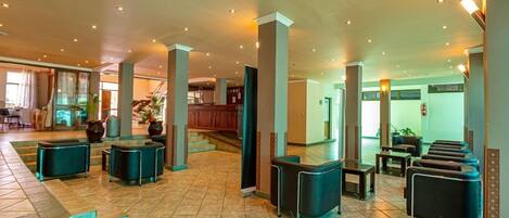 A spacious lobby with a high ceiling, multiple seating areas, and a staircase leading to upper floors.