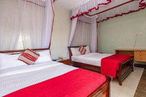 Habitación de hotel con dos camas, cada una con dosel y ropa de cama roja. Se observa un mesita de noche de madera con un teléfono y una pequeña mesa con una lámpara.
