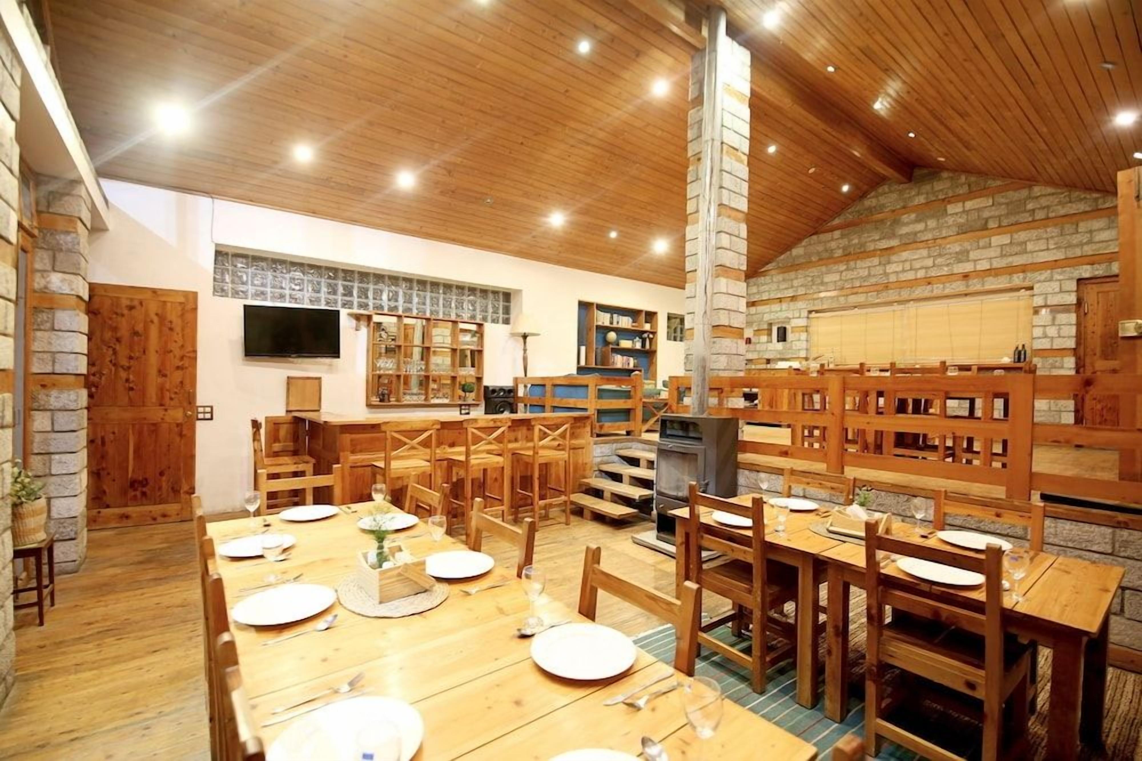 A dining area with wooden tables and chairs, a stone fireplace, and a television mounted on the wall.