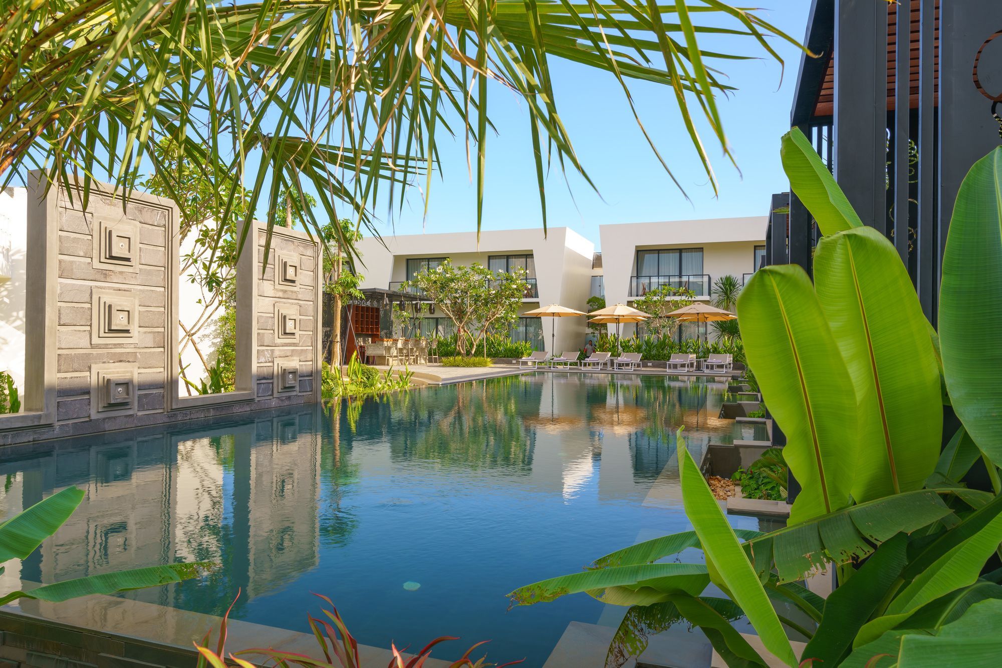 A swimming pool with lounge chairs and umbrellas, surrounded by greenery and modern buildings.