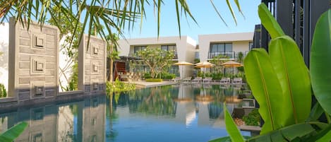 Piscina com espreguiçadeiras e guarda-sóis, cercada por vegetação e edifícios modernos.
