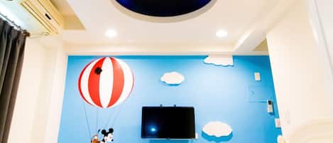 Habitación de hotel con una cama grande, un televisor de pantalla plana montado en la pared y un diseño en el techo que recuerda a las orejas de Mickey Mouse.