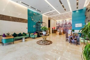 Un lobby moderno con una pared de acento color aguamarina, una recepción y un área de descanso con una mesa redonda y sillas.