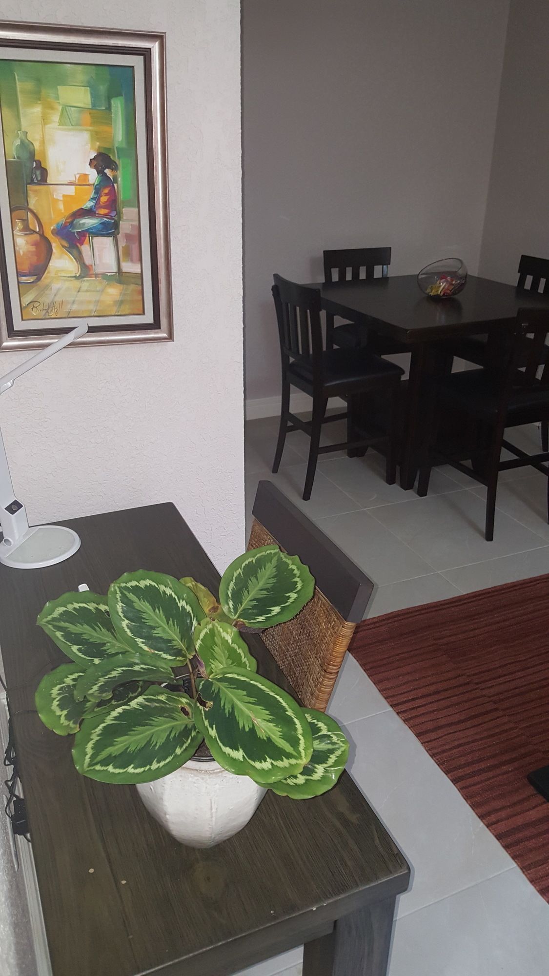 Un coin repas comprenant une table, des chaises, une plante en pot et un tableau accroché au mur.