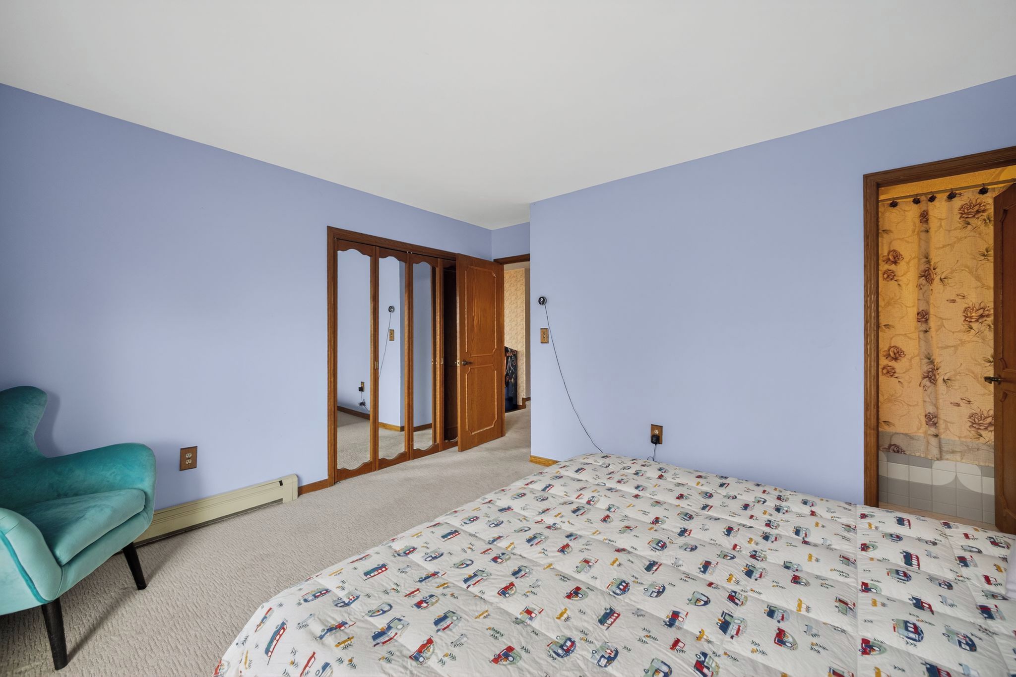A bedroom with a bed, a chair, a wardrobe, and a door with a floral pattern.
