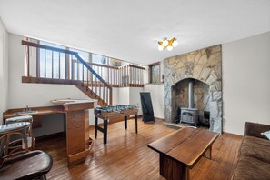 Una habitación amplia con una mesa de madera, una mesa de fútbol de mesa, una chimenea de piedra y una escalera con barandillas de madera.