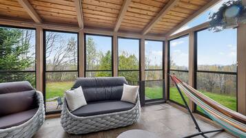 A sunroom with a cushioned seating area, large windows, and a hammock.