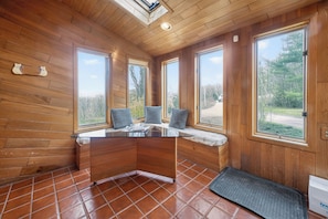 A wooden cabin interior with a glass-top table, large windows, and a tiled floor.