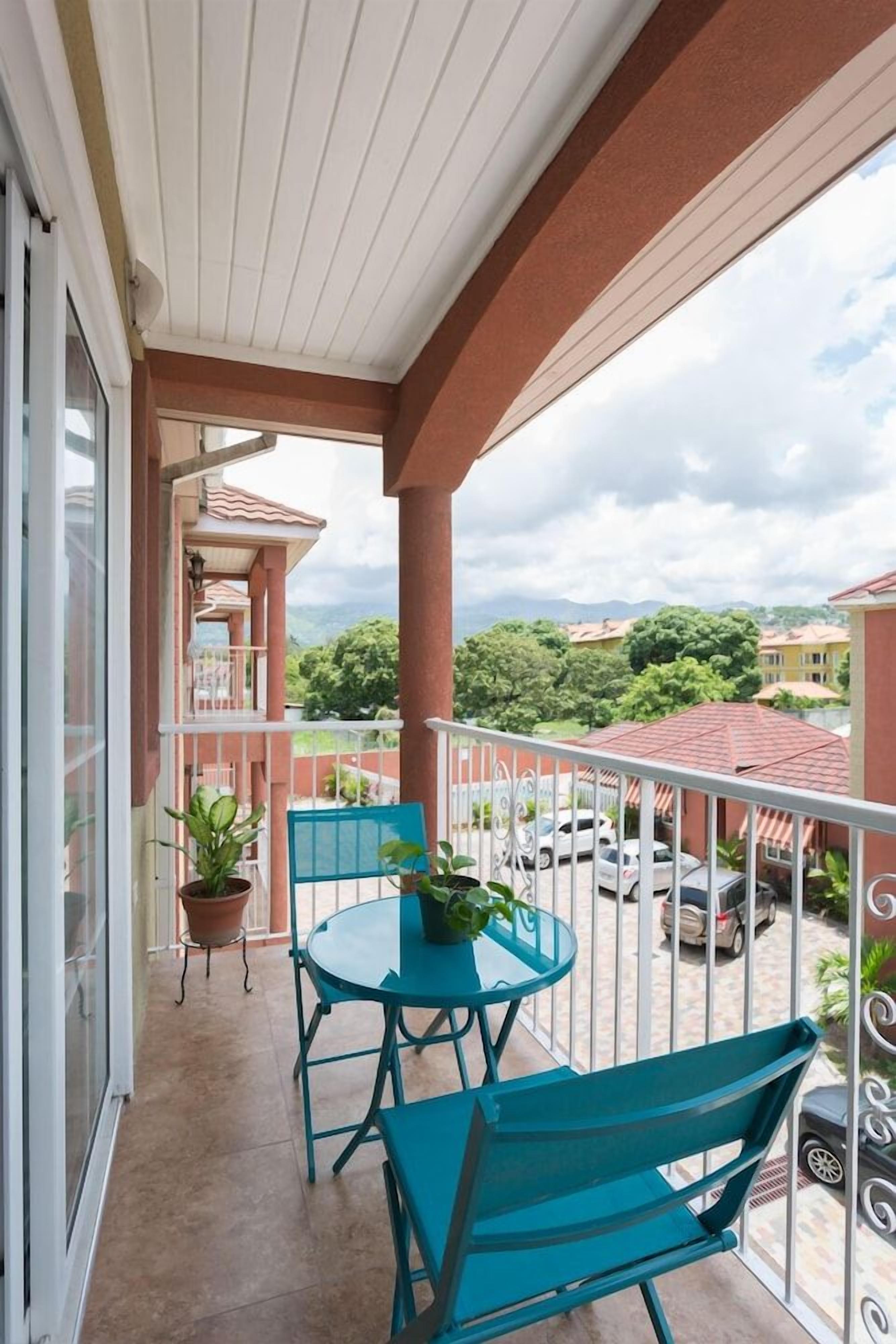 A balcony with a table and chairs, potted plants, and a view of a residential area.