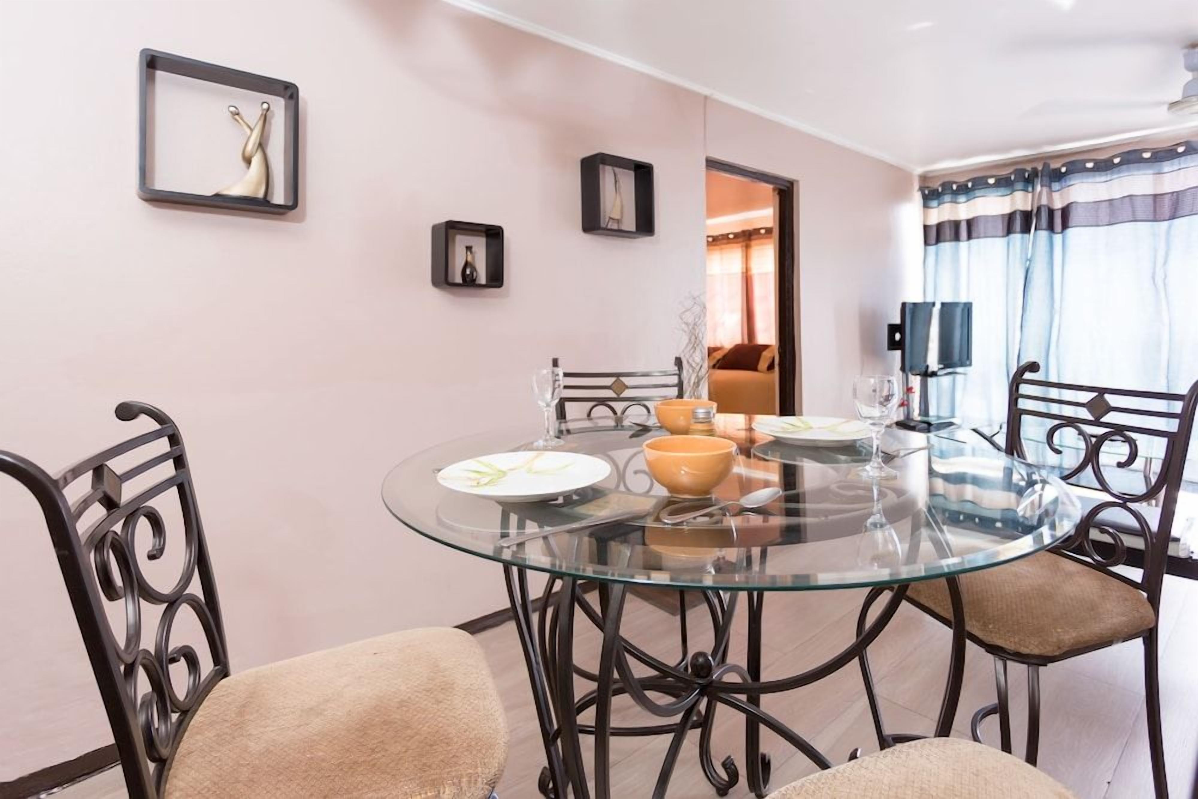 A dining area with a glass table, metal chairs, and a view into another room.