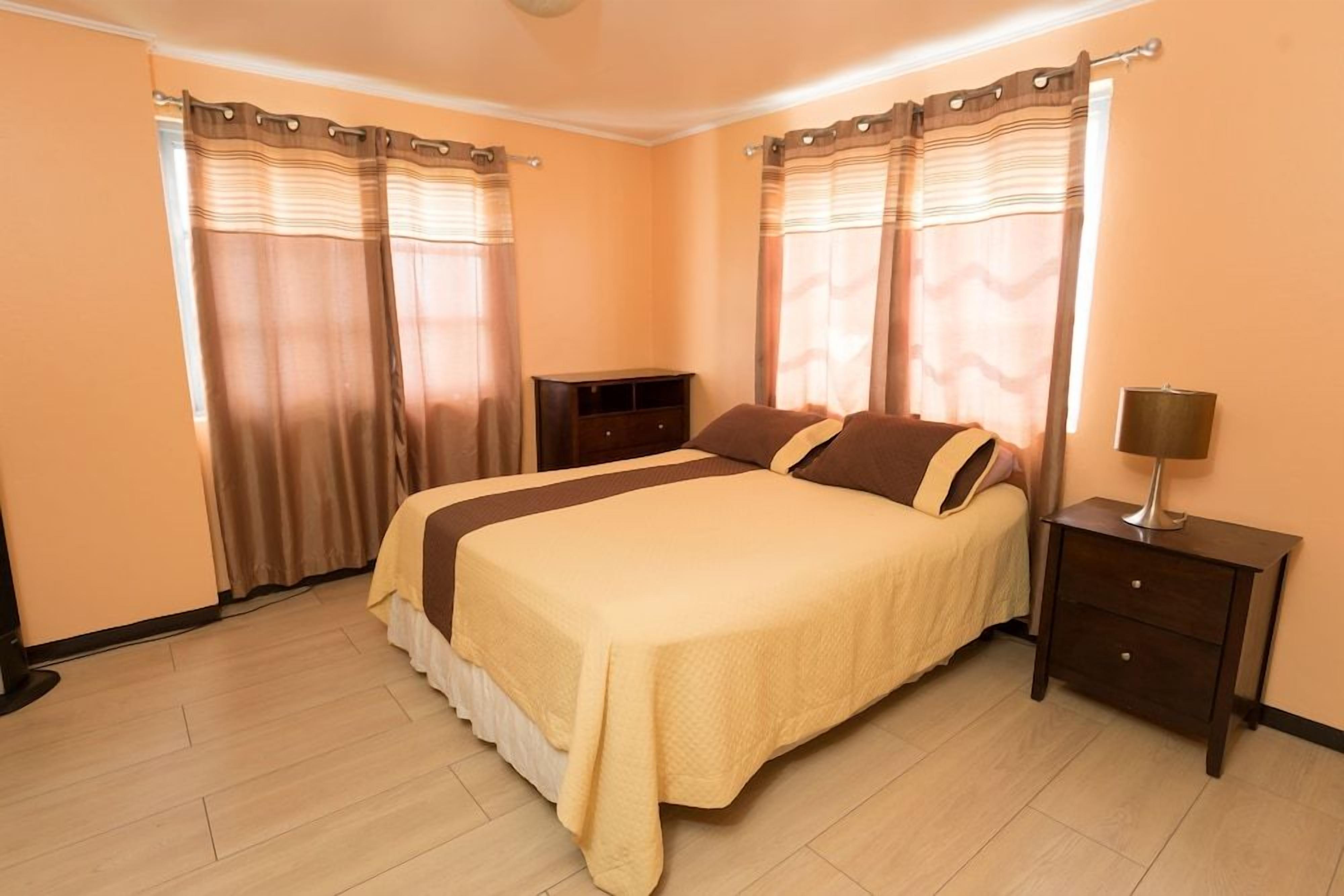 A bedroom with a bed, curtains, a nightstand, and a dresser.