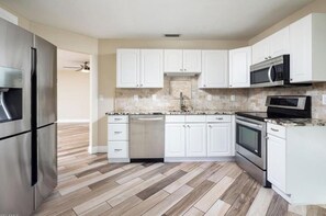 Une cuisine moderne dotée d’appareils électroménagers en acier inoxydable, de meubles blancs et d’un parquet en bois disposé en motif chevrons.