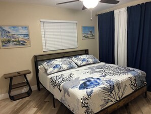 Une chambre à coucher avec un lit, un ventilateur de plafond, une fenêtre avec des stores et une table de chevet.