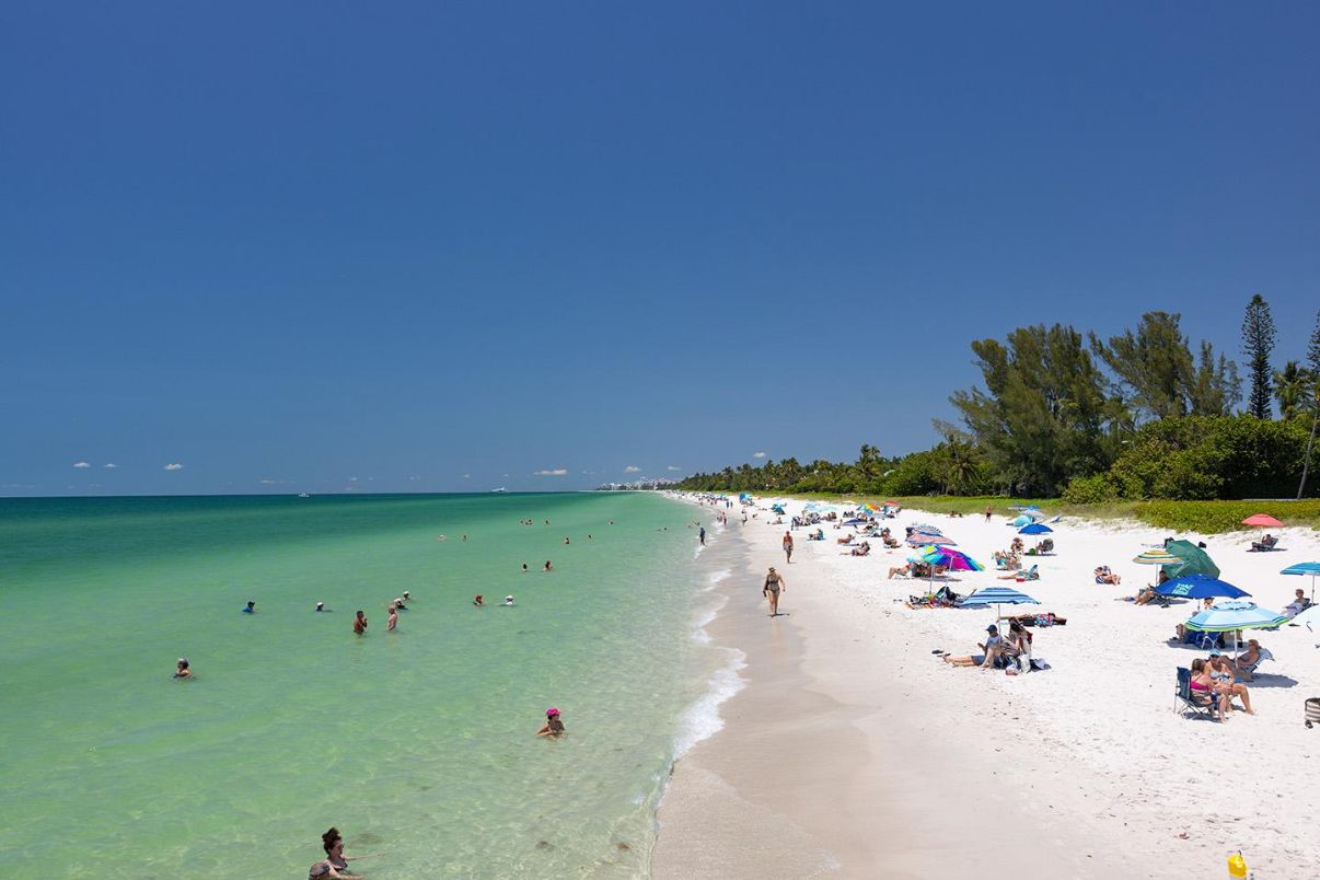 A beach with clear turquoise water, people swimming and sunbathing, and umbrellas on the sand.