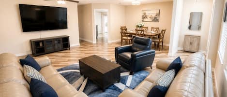 A living room with a flat-screen TV, leather sofas, a coffee table, and a dining area with chairs and a table.