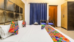 A hotel room with a large bed, a headboard, a blue curtain, a wooden wardrobe, and a small table with a chair. - Fabhotel The Residency DLF Galleria (Gurugram)