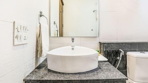 A bathroom with a round sink, a mirror, a towel rack, and a shower area. - Fabhotel The Residency DLF Galleria (Gurugram)