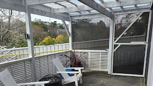 Ein überdachter Außenbereich mit zwei Adirondack-Stühlen, einem Blumentopf und einer Bank.