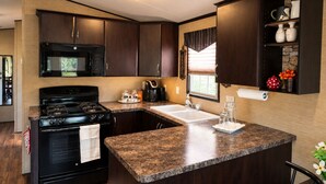 Cocina compacta con alacenas de madera oscura, estufa negra, microondas y encimera de granito.