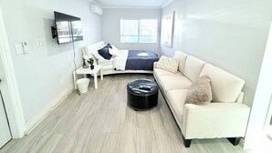 A modern, well-lit room with a bed, a sofa, a small table, and a television mounted on the wall. - Cozy 1-bedroom & 2beds house in Rowland Heights with AC near Disneyland Park (Rowland Heights)