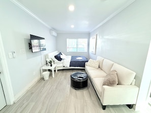 Quarto moderno e bem iluminado com cama, sofá, mesinha e televisão fixada na parede.