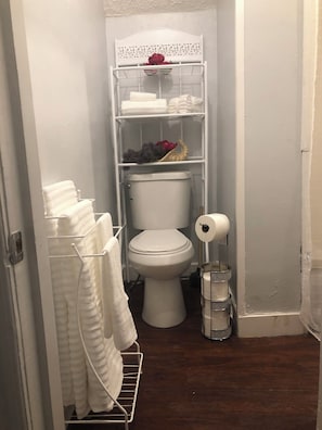 Une petite salle de bain comprenant des toilettes, une étagère avec des serviettes et un porte-rouleau de papier toilette.