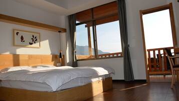 A bedroom with a wooden bed, a large window, a balcony, and a framed artwork on the wall.