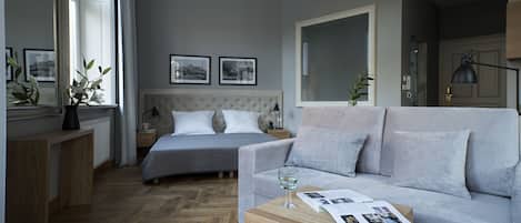 A modern bedroom with a bed, a grey sofa, a wooden coffee table, and a mirror.