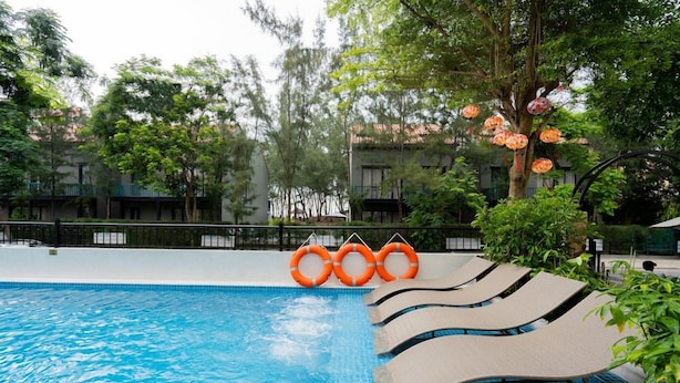 Una piscina con superficie de agua azul cristalina, rodeada de sillas de descanso y flotadores anaranjados.
