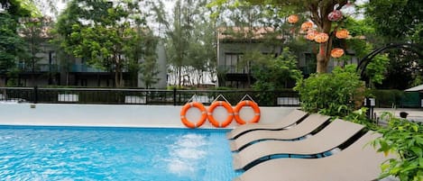 A swimming pool with a clear blue water surface, surrounded by lounge chairs and orange life rings.