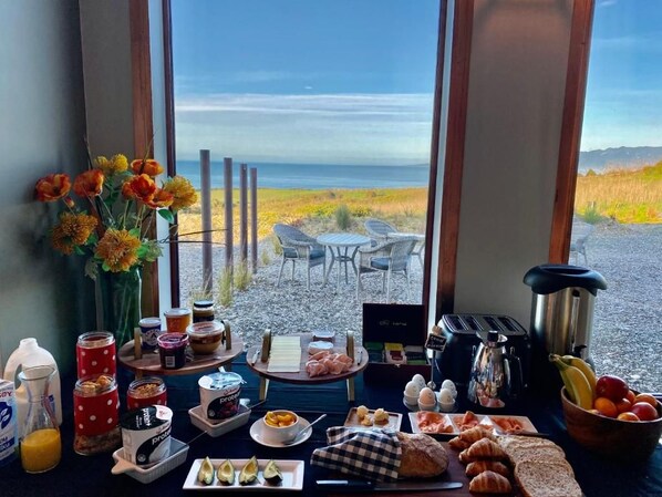 A breakfast buffet with various food items and a view of the beach. - The Cliffs Seaside Lodge (Papatotara)