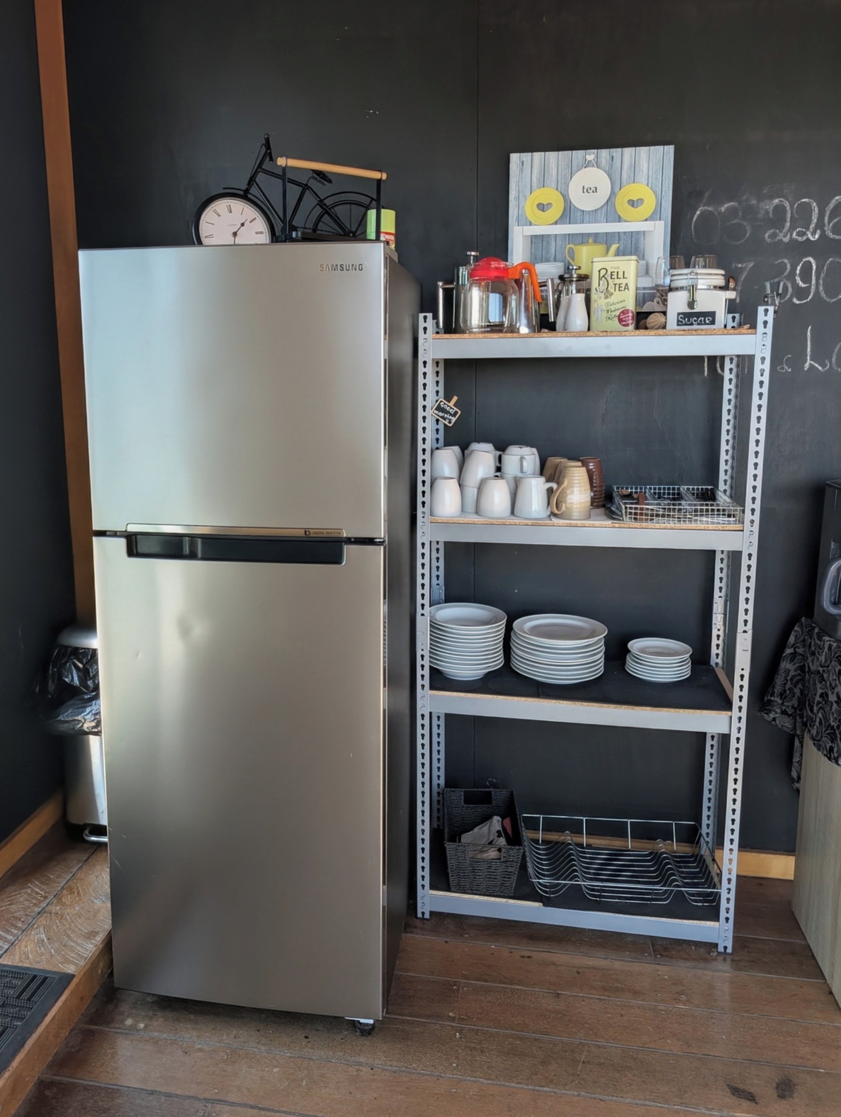 A stainless steel refrigerator, a shelf with kitchenware, and a chalkboard with writing.