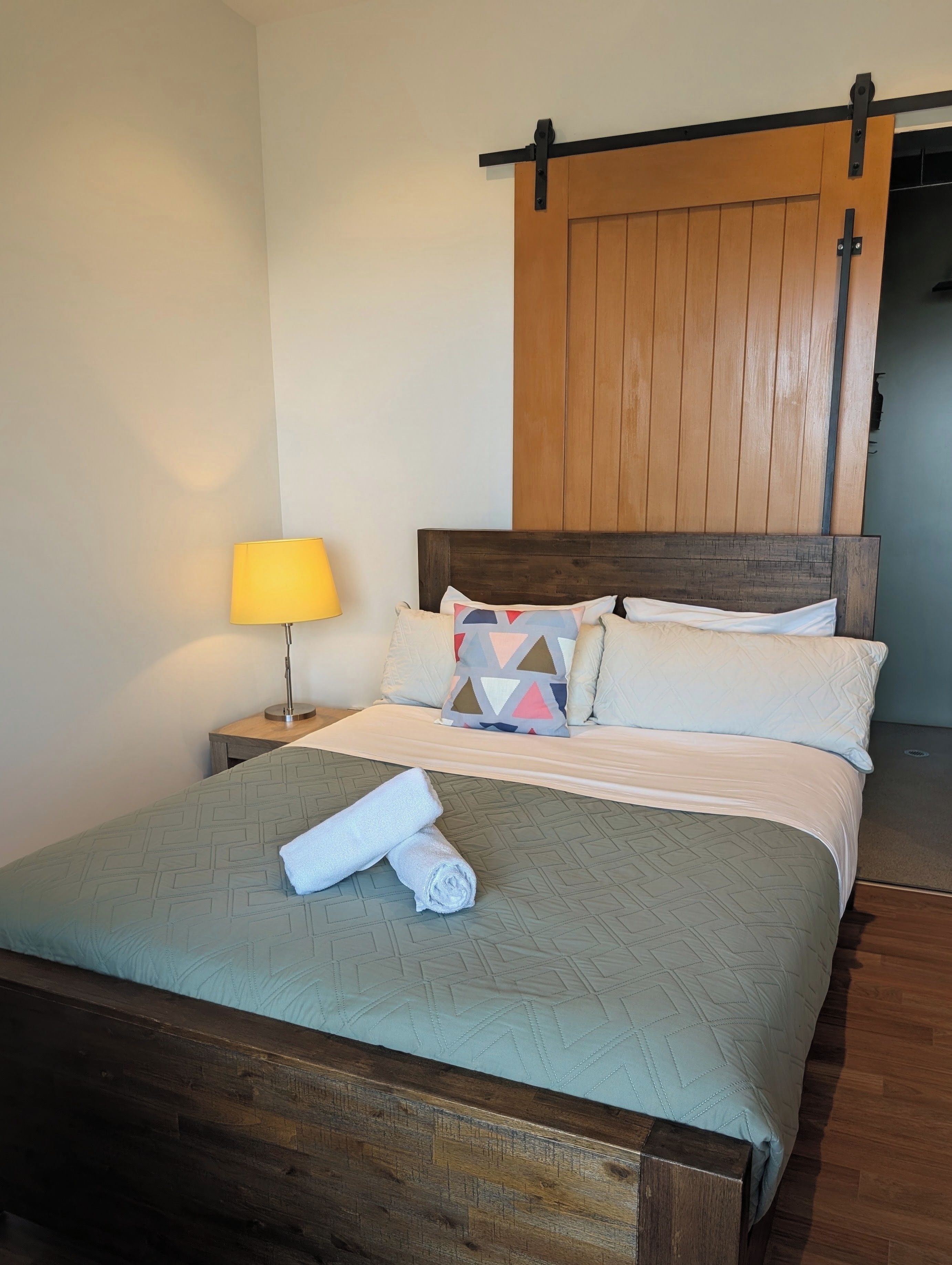 Un lit avec une couvre-lit à motifs géométriques, une serviette enroulée et un oreiller orné d’un motif géométrique.
