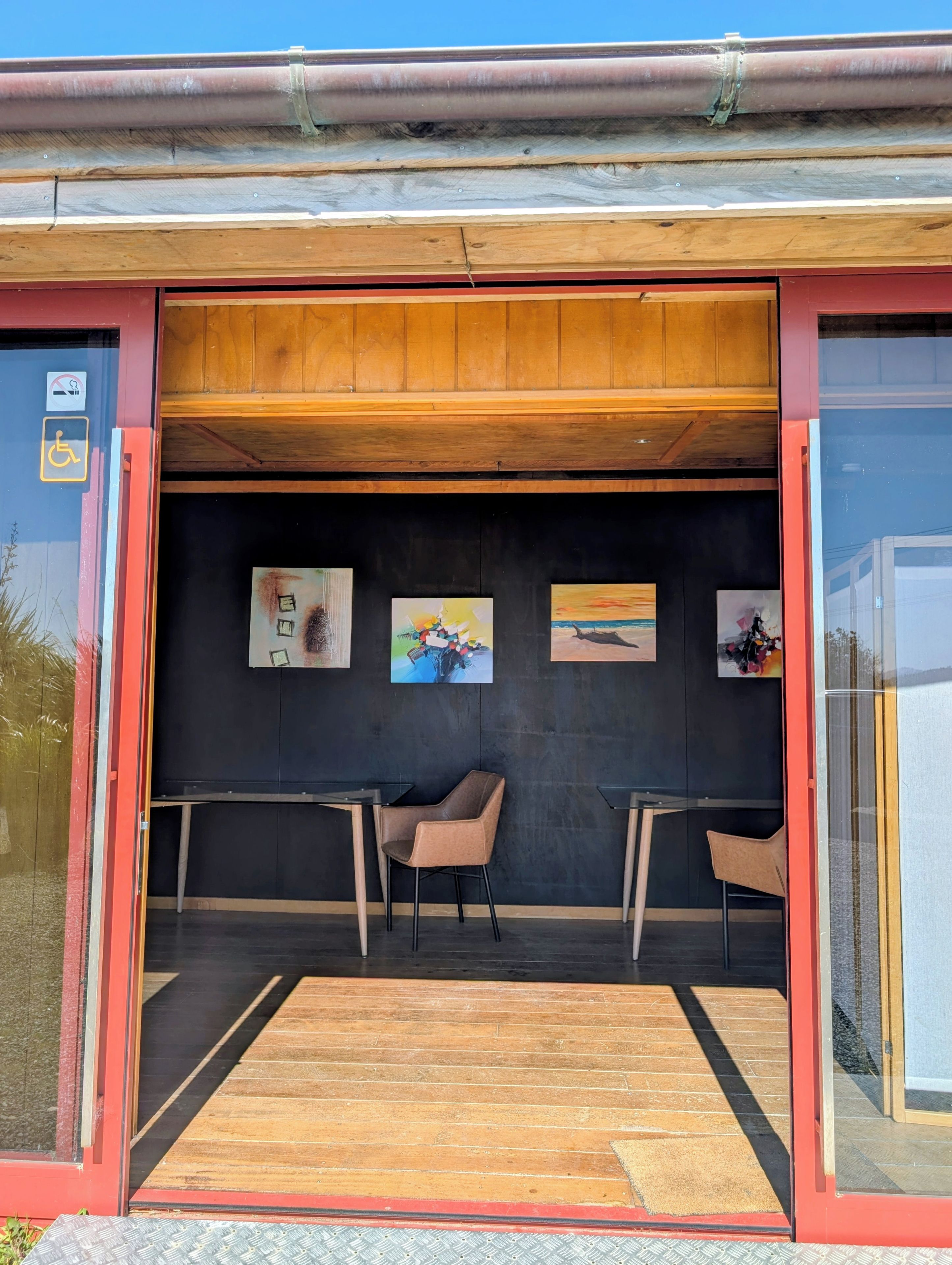 An entrance with a wooden ceiling, black walls, and a black floor. There are two chairs and a small table.