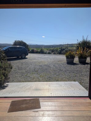 A view from a room's entrance to a gravel driveway with a parked car, potted plants, and a clear sky. - The Cliffs Seaside Lodge (Papatotara)