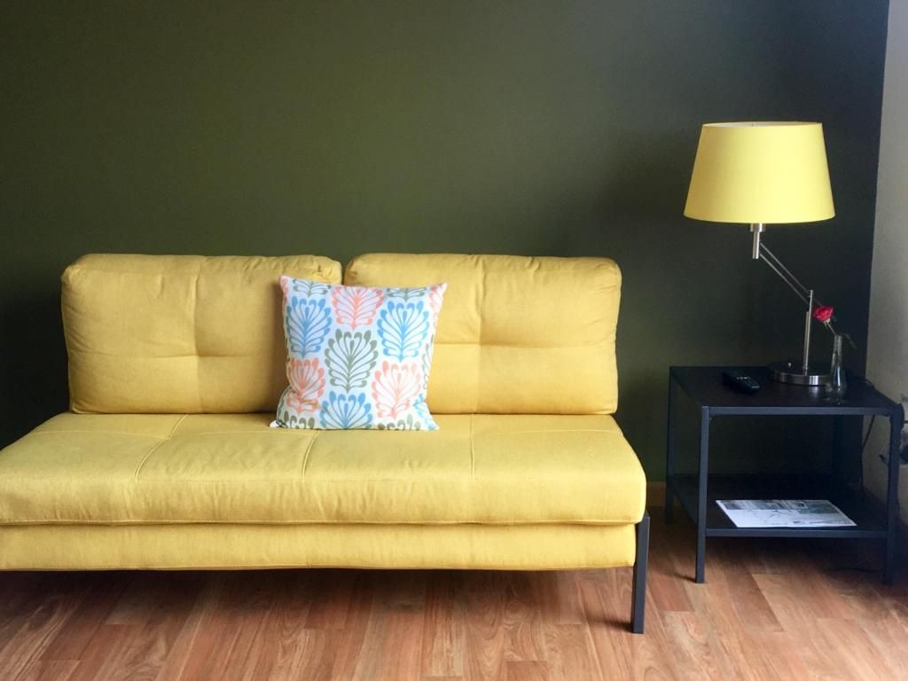 A yellow sofa with a patterned pillow, a black side table with a lamp, and a magazine on the table.