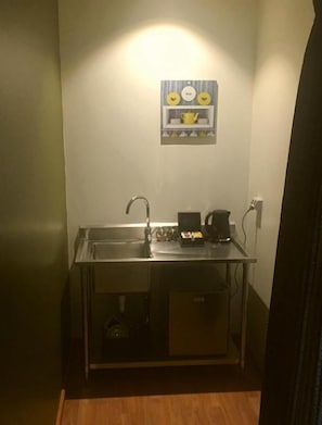 A compact kitchenette with a sink, a coffee maker, and a small cabinet.