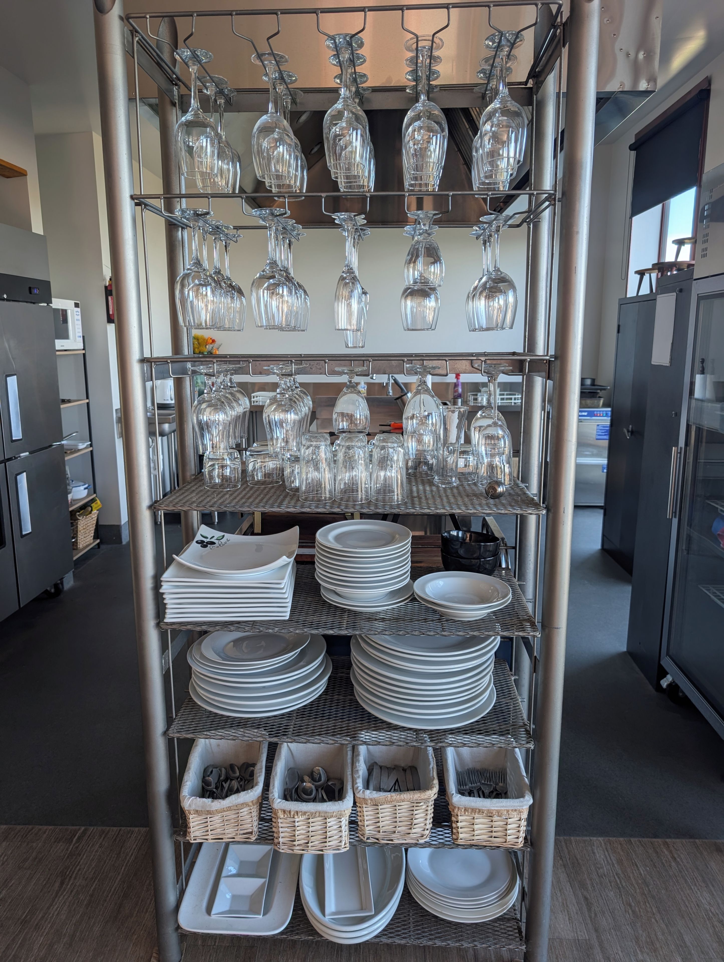 A kitchen with stainless steel appliances, a wine rack with multiple glasses, and neatly stacked plates and bowls.