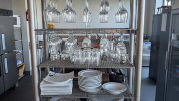 A kitchen with stainless steel appliances, a wine rack with multiple glasses, and neatly stacked plates and bowls.