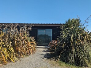 A pathway leading to a modern building with a glass door and a metal roof. - The Cliffs Seaside Lodge (Papatotara)