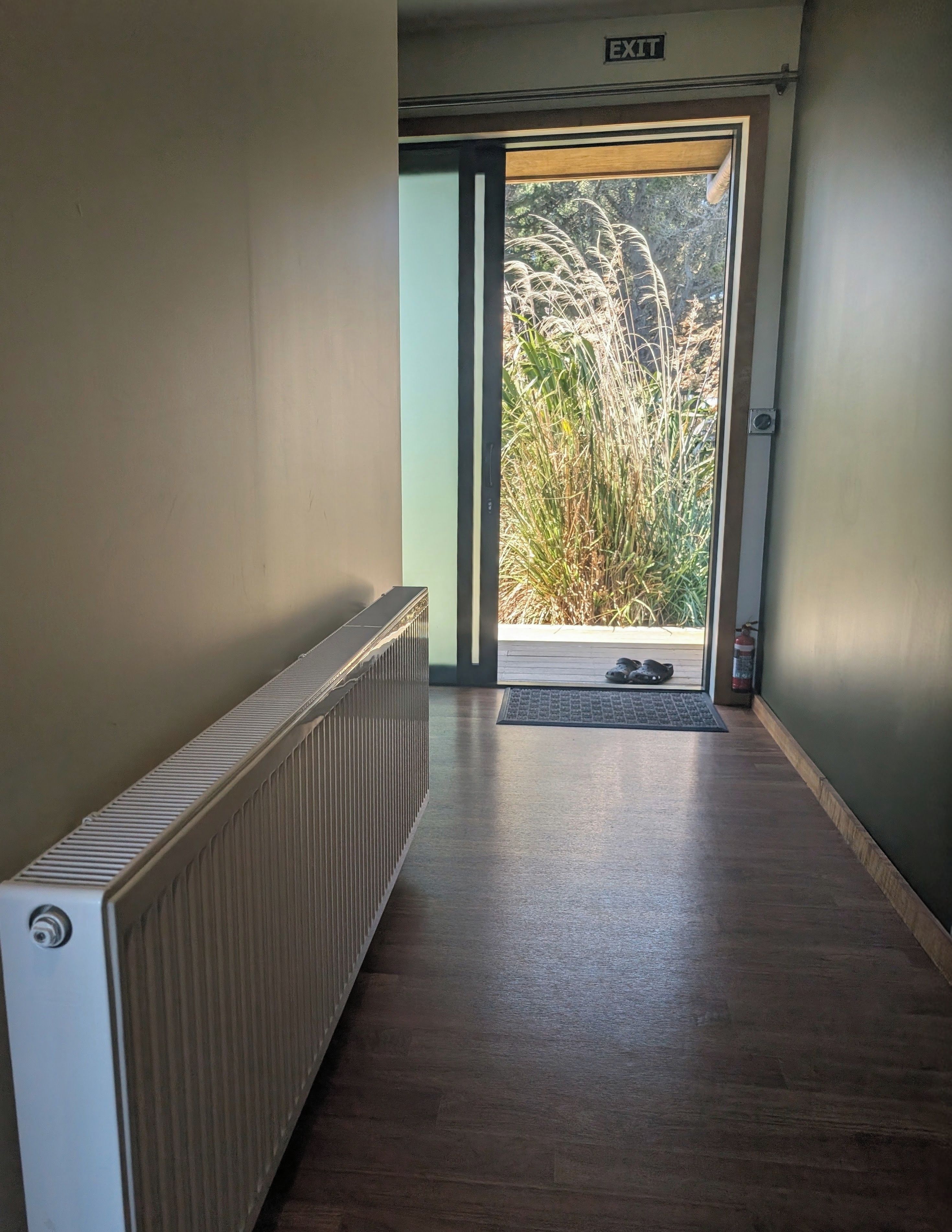 Un couloir avec un radiateur, une porte donnant sur l’extérieur et un paillasson à l’entrée.