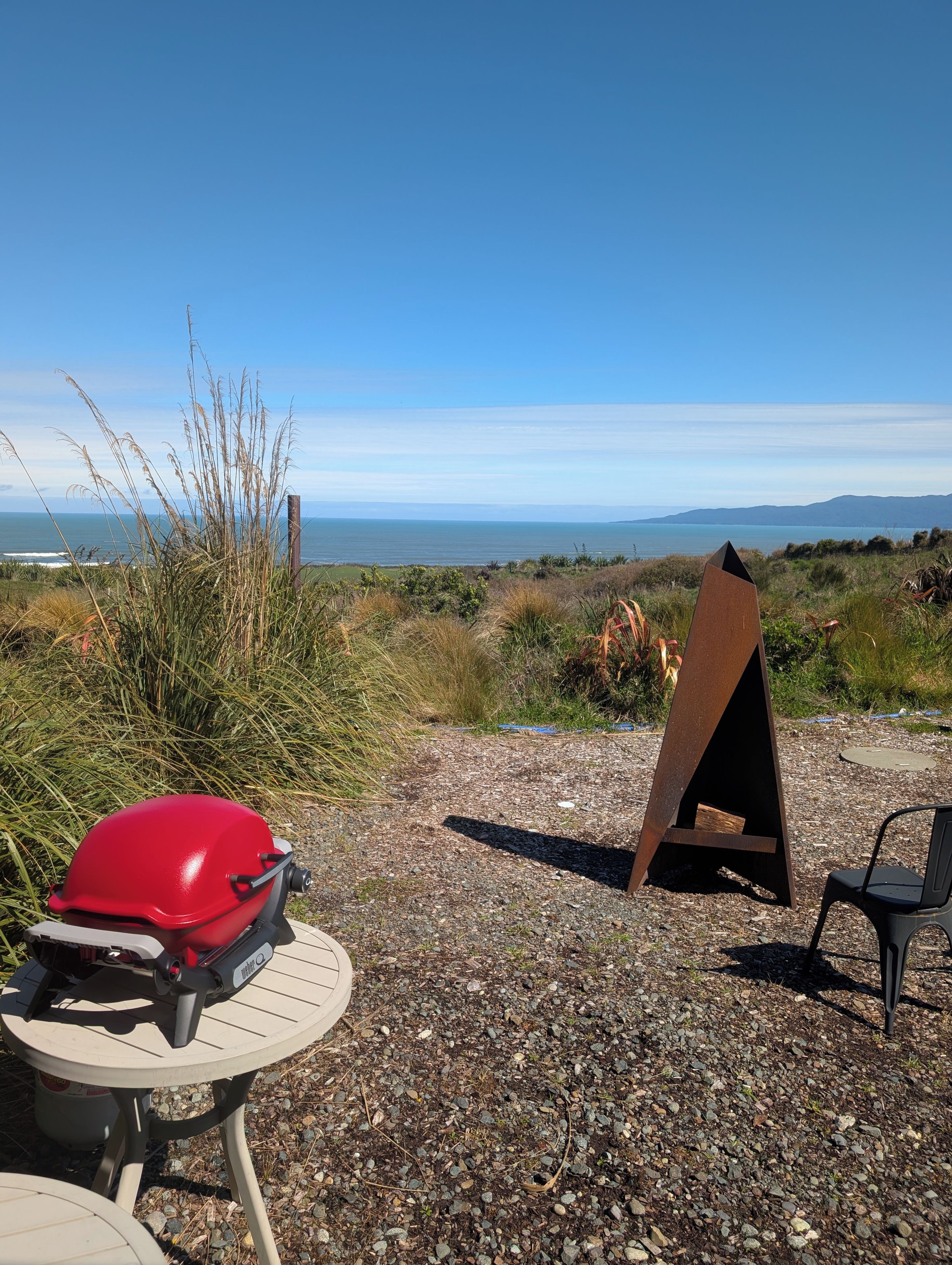 A gravel area with a red grill, a black chair, and a metal A-frame structure.