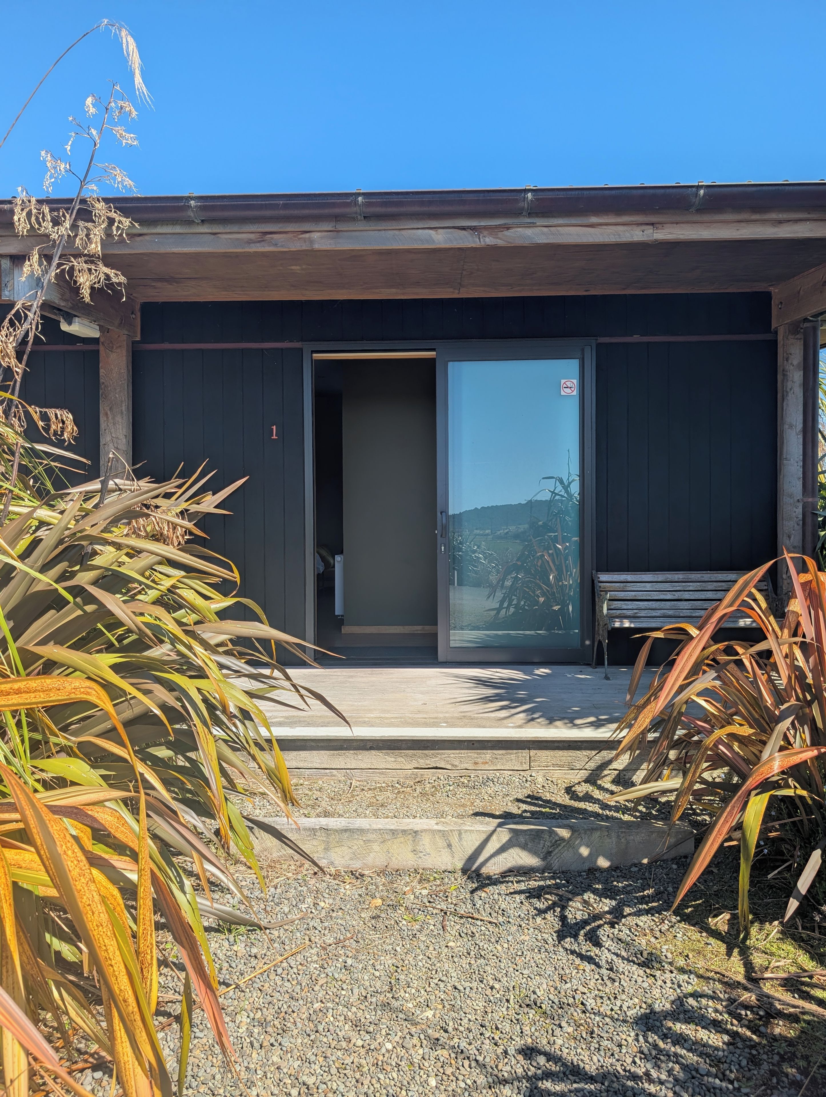 A modern building with a large glass door, a bench, and a gravel pathway.