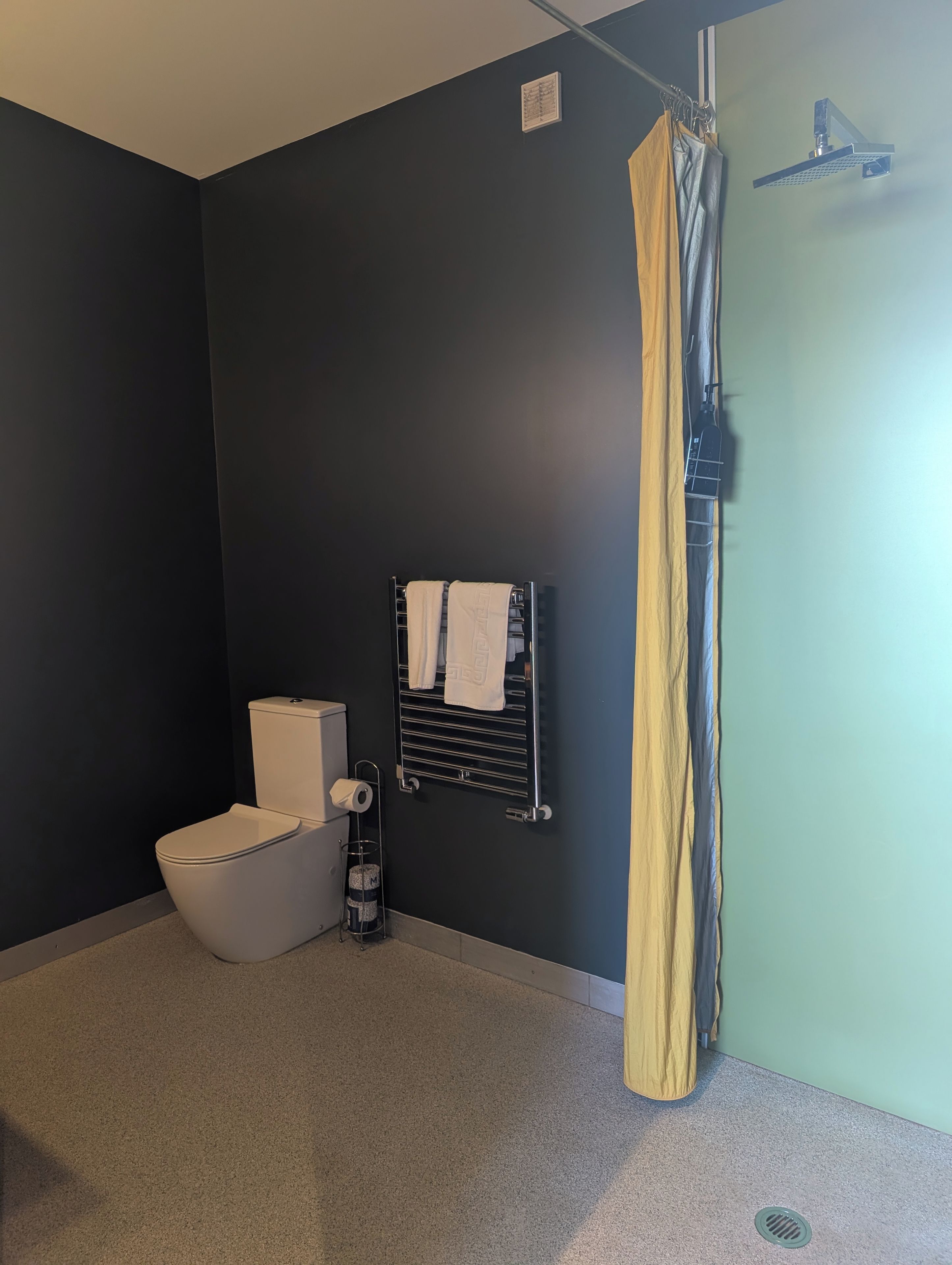 A bathroom with a toilet, a towel rack with towels, a shower curtain, and a toilet paper holder.