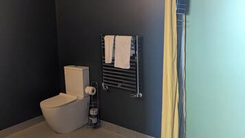 A bathroom with a toilet, a towel rack with towels, a shower curtain, and a toilet paper holder.