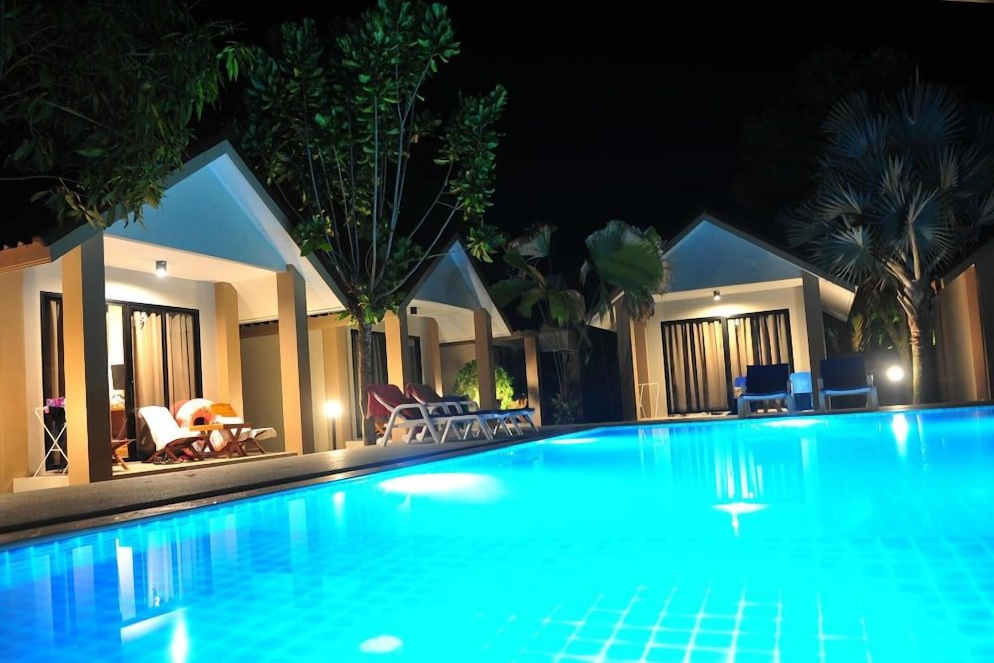 A swimming pool with lounge chairs and umbrellas, surrounded by palm trees and a night sky.