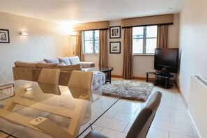 A modern living room with a sofa, a glass coffee table, a TV, and a fireplace. - Posh Pads at The Casartelli (Liverpool)