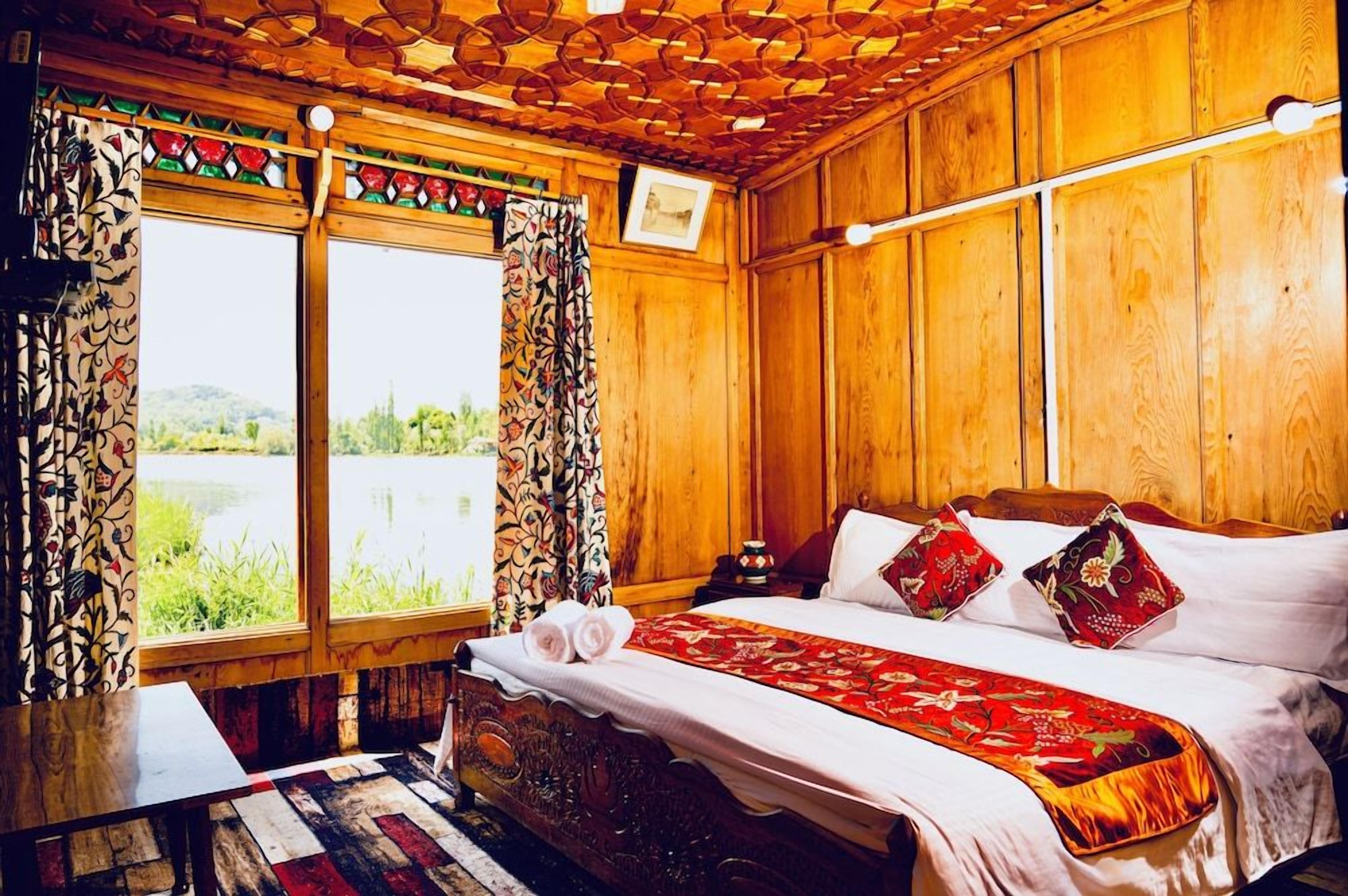 Quarto de madeira com cama, cortinas e vista para o verde.