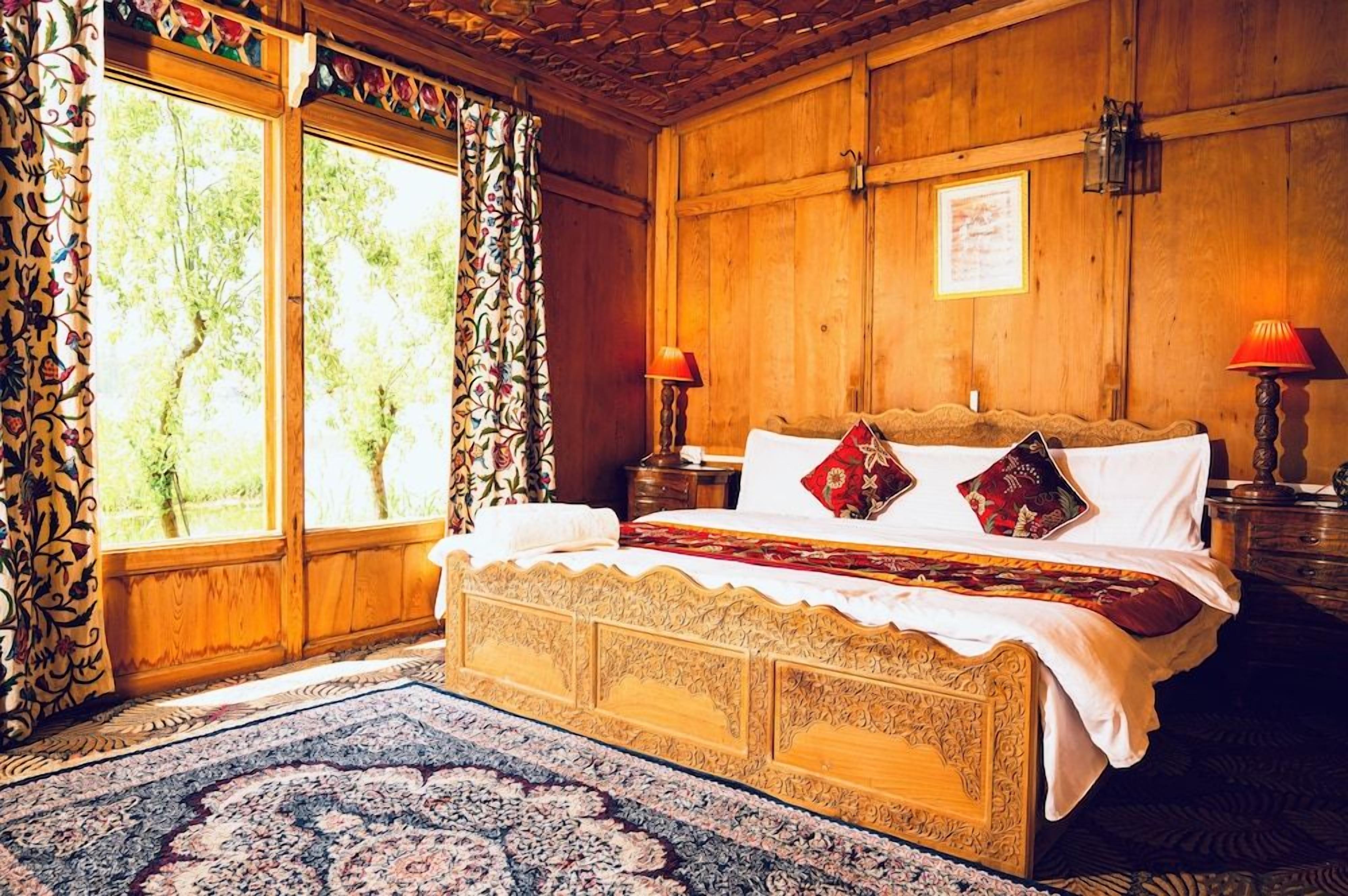 Quarto de madeira tradicional com uma cama grande, duas mesas de cabeceira e uma janela com cortinas.
