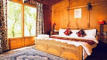 Quarto de madeira tradicional com uma cama grande, duas mesas de cabeceira e uma janela com cortinas.